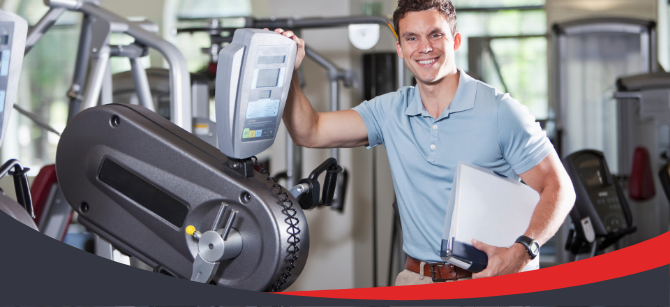 Physiotherapist adjusting a rehabilitation exercise machine while holding a clipboard in a modern clinic gym.