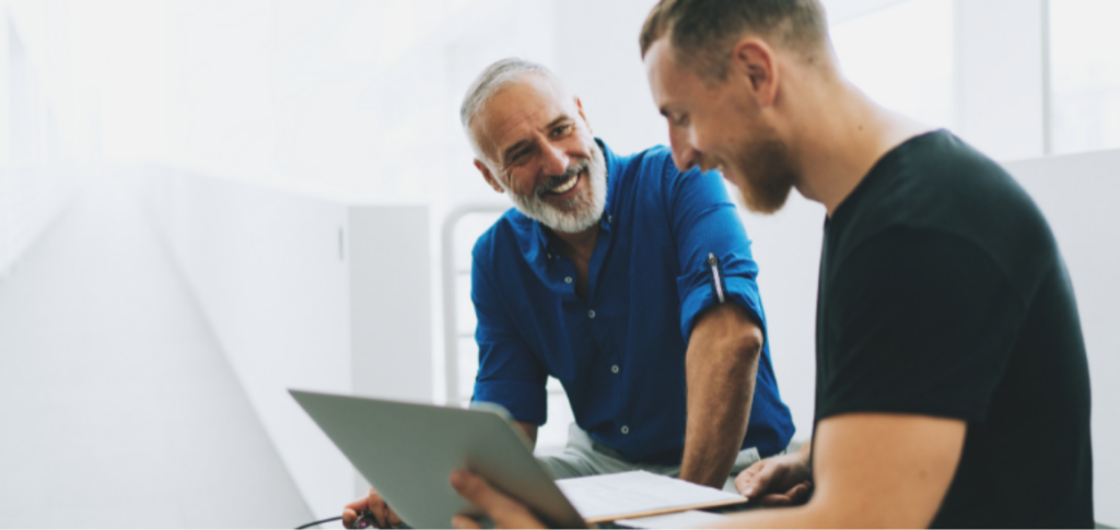 Two men speaking and laughing in front of a computer